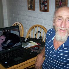 Art on his computer at the kitchen table surrounded with pictures of he grandchildren
