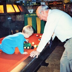 Arvin showing grandson, Sam, how to play on the pool table of his Coal Valley, IL, home with a John Deere skid steer and pool balls (1991).