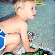Sam Lukas (1991), playing with the new John Deere tractors and books from grandparents' Arvin & Bev for his birthday at the lake home.