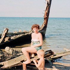 Mom sitting on boat wreck with Steve, 1950s.