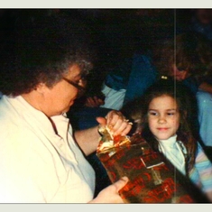 62 - Mammaw with her granddaughter Sarah opening presents at the annual Christmas party circa 1980s