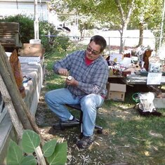 Brian carving on one of his walking sticks while having a yardsale