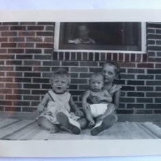 Summer on the front porch; Vicki, Linette holding Denny, with Lester peaking through the window.