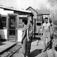 Mom standing back to back with our neighbor Pearl's son to see how much he had grown. Dad our working fixing our humble home.