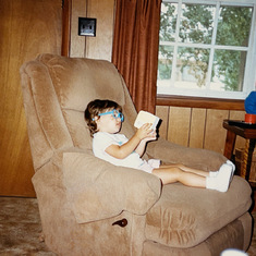 Jennie "reading" in dad's recliner. I couldn't read at the time, but I would put on my blue glasses, sit in his chair and recite the stories from memory. 