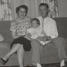 Claudia (1 yr) sitting w Mom & Dad Nov 1957