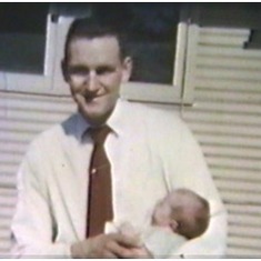 Tom holding baby Shannon at the 'Huts,' St. Thomas College, summer 1957 (still from family movie)