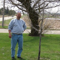 Wayne in ND standing by his friend Kenny's Tree planted in memory of him on our property there.